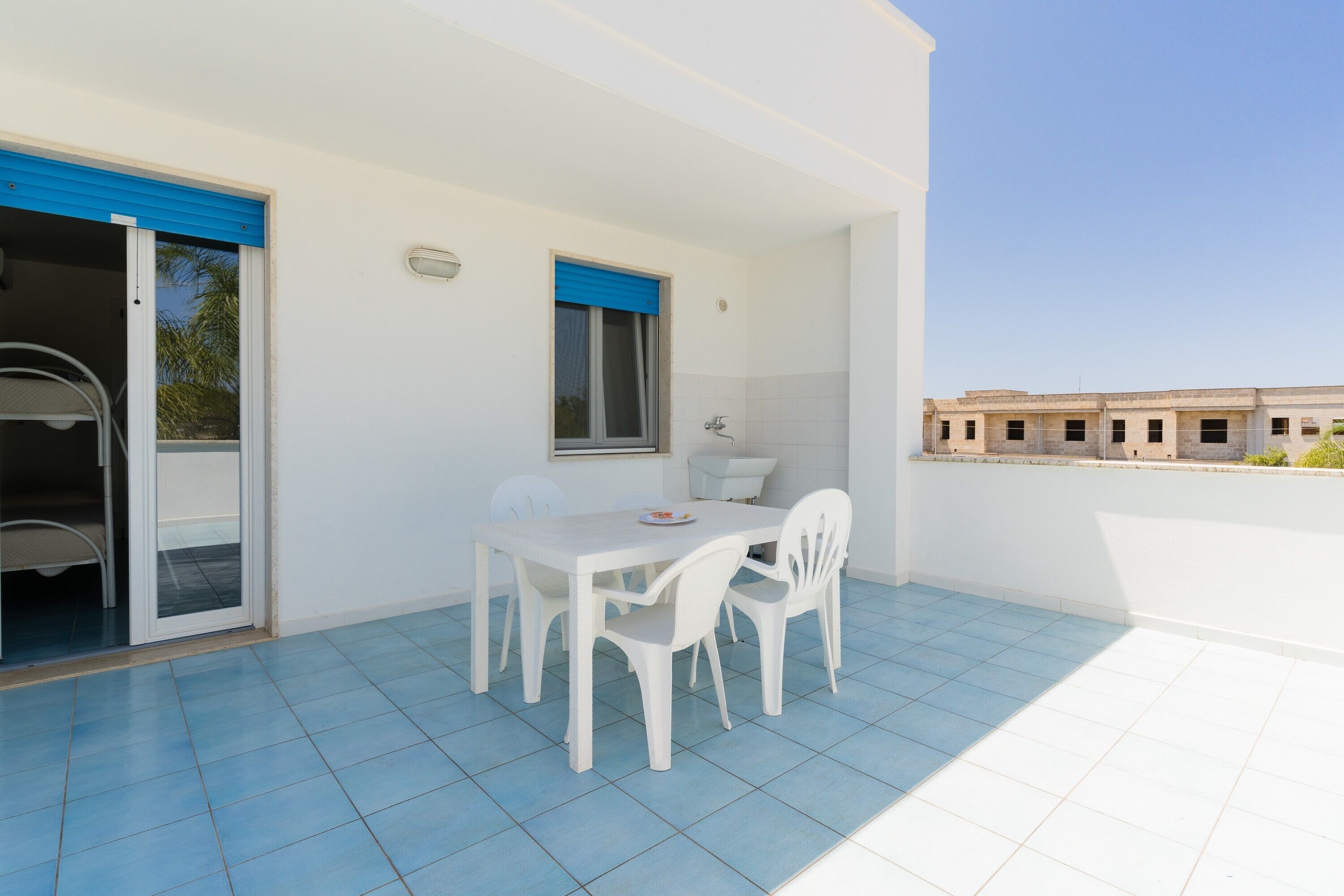 Un patio con tavolo e sedie, una porta scorrevole e vista su un edificio sullo sfondo.