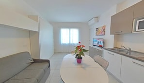 Un espace de vie compact comprenant un coin cuisine, un coin repas avec une table et des chaises, un canapé et une plante en pot.