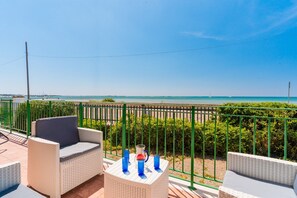 Ein Balkon mit Korbmöbeln, einem Tisch mit blauen Gläsern und Blick auf das Meer.