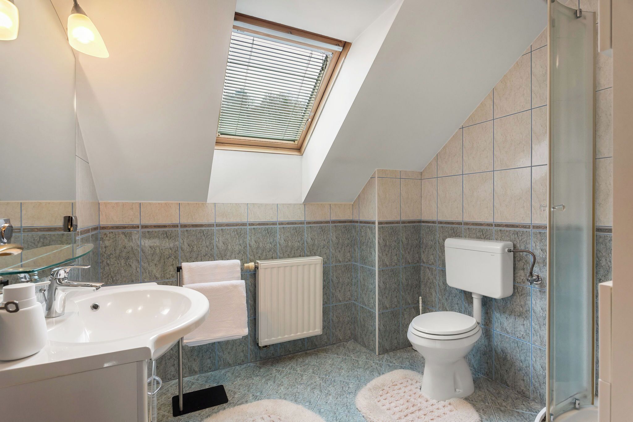 A modern bathroom with a skylight, a sink, a toilet, and a glass shower enclosure.