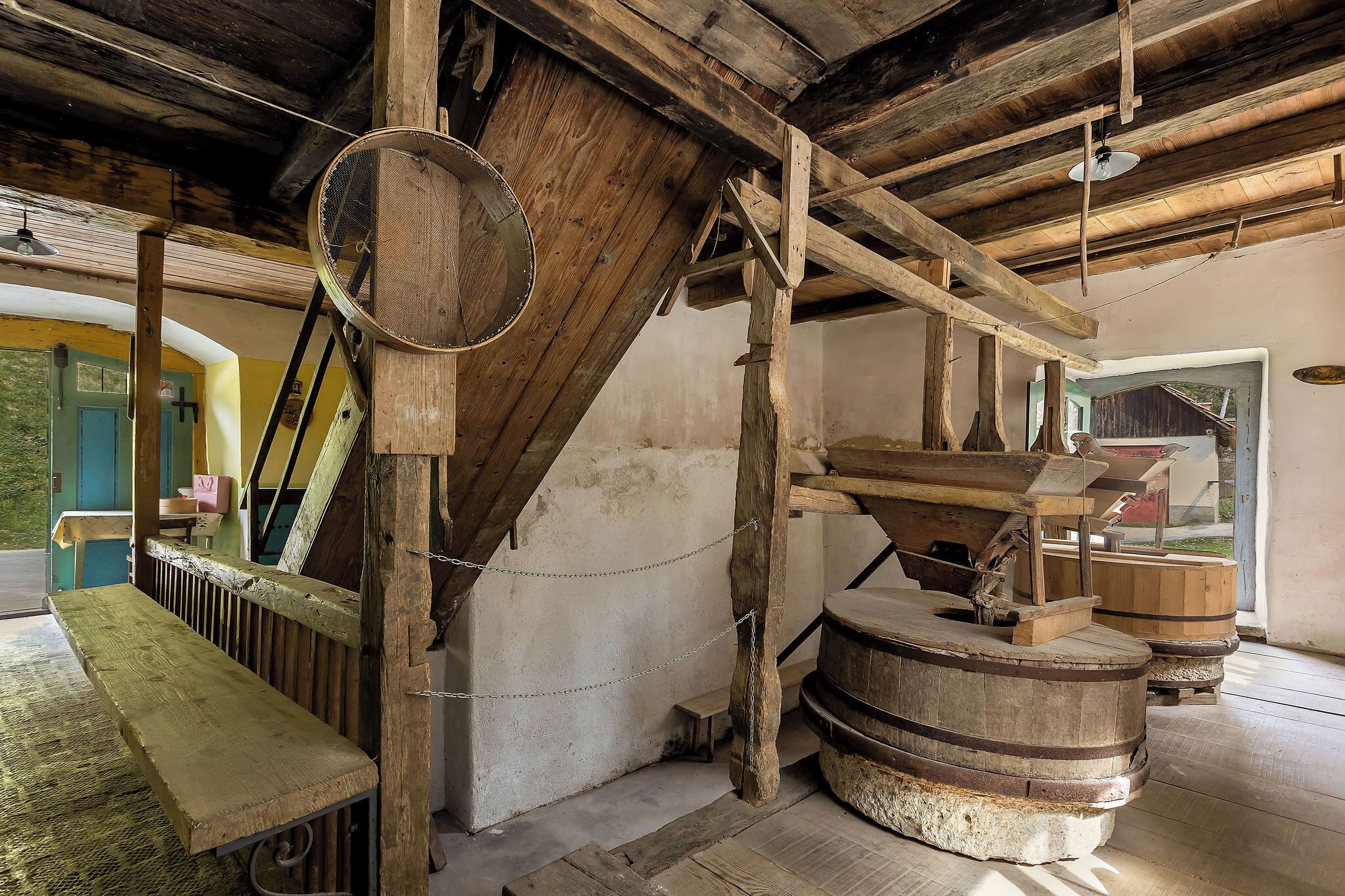 Un interior rústico con vigas de madera, un banco de madera y un barril grande de madera.