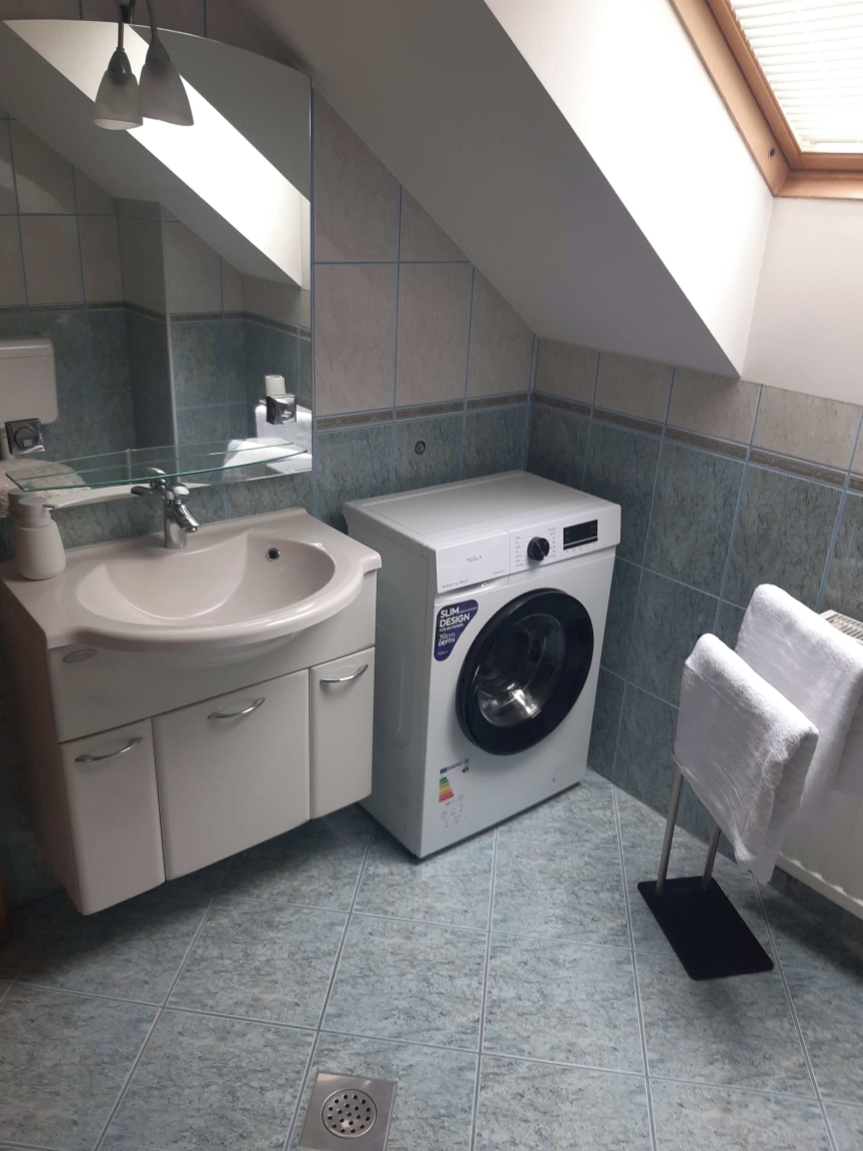 A compact bathroom with a sink, mirror, and a front-loading washing machine.