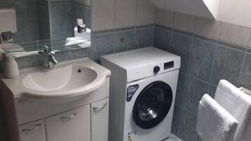 A compact bathroom with a sink, mirror, and a front-loading washing machine.