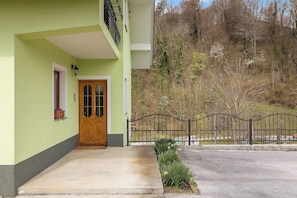 A house with a green exterior, a wooden front door, a small window with a flower box, and a black wrought iron gate.
