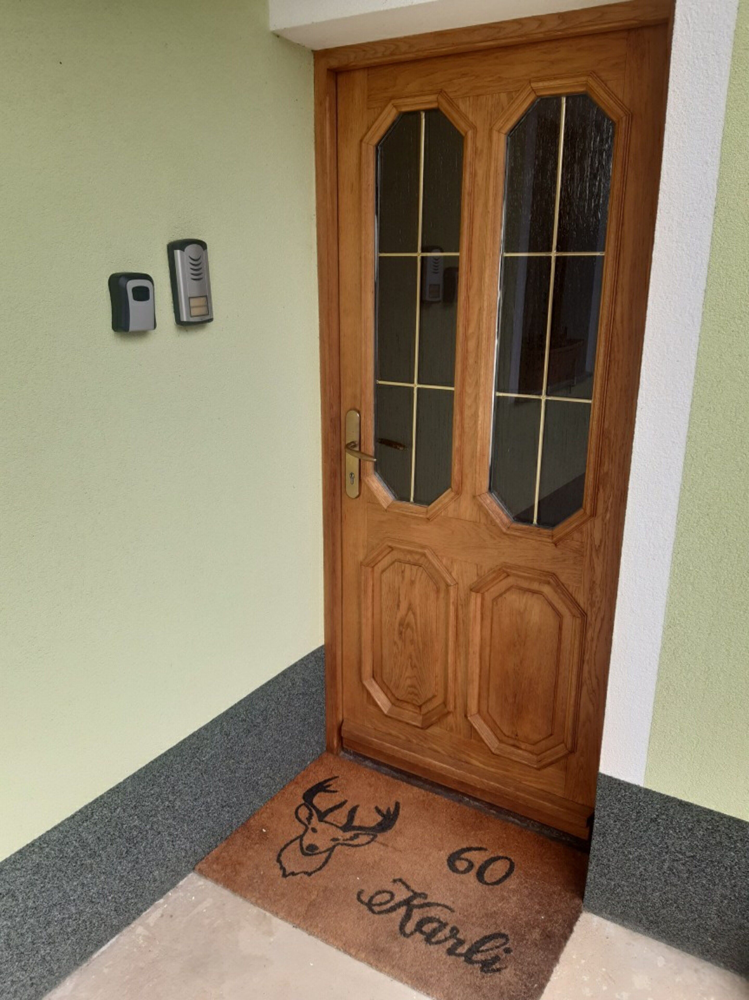 A wooden door with a glass panel, a doorbell, and a doormat with a deer head and the number 60.