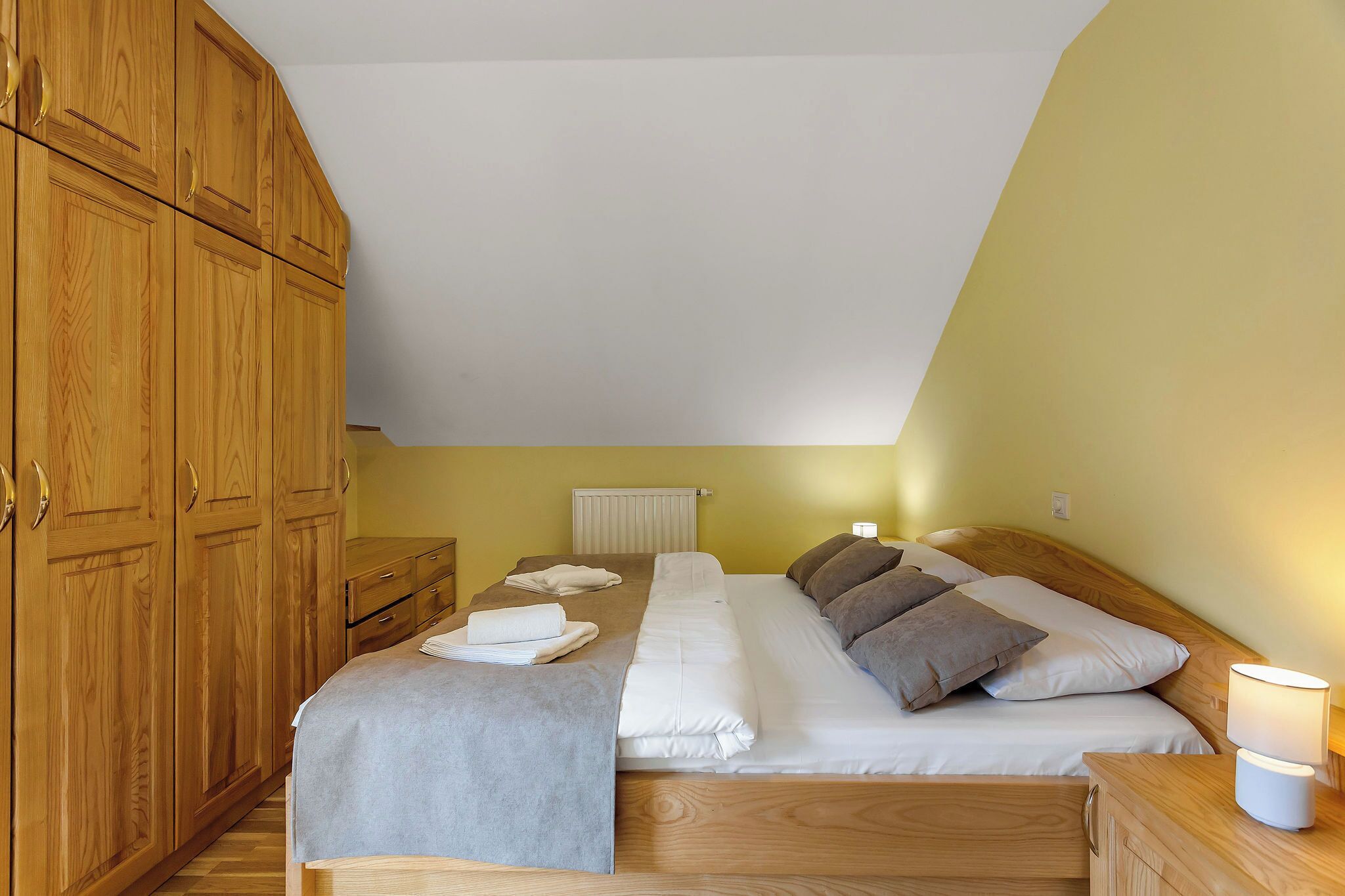 Ein Schlafzimmer mit Bett, Holzschrank und Nachttisch mit Lampe.