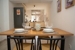 Ein Essbereich mit einem Holztisch, gedeckt für zwei Personen, schwarzen Stühlen, einem dekorativen Blumenarrangement und einer Küche im Hintergrund.