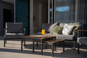 Ein Sitzbereich im Freien mit einer Couch, zwei Stühlen und einem Tisch mit einem Glas Orangensaft.