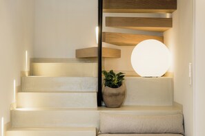 Un escalier avec un luminaire rond, une plante en pot et une marche recouverte d’un coussin.