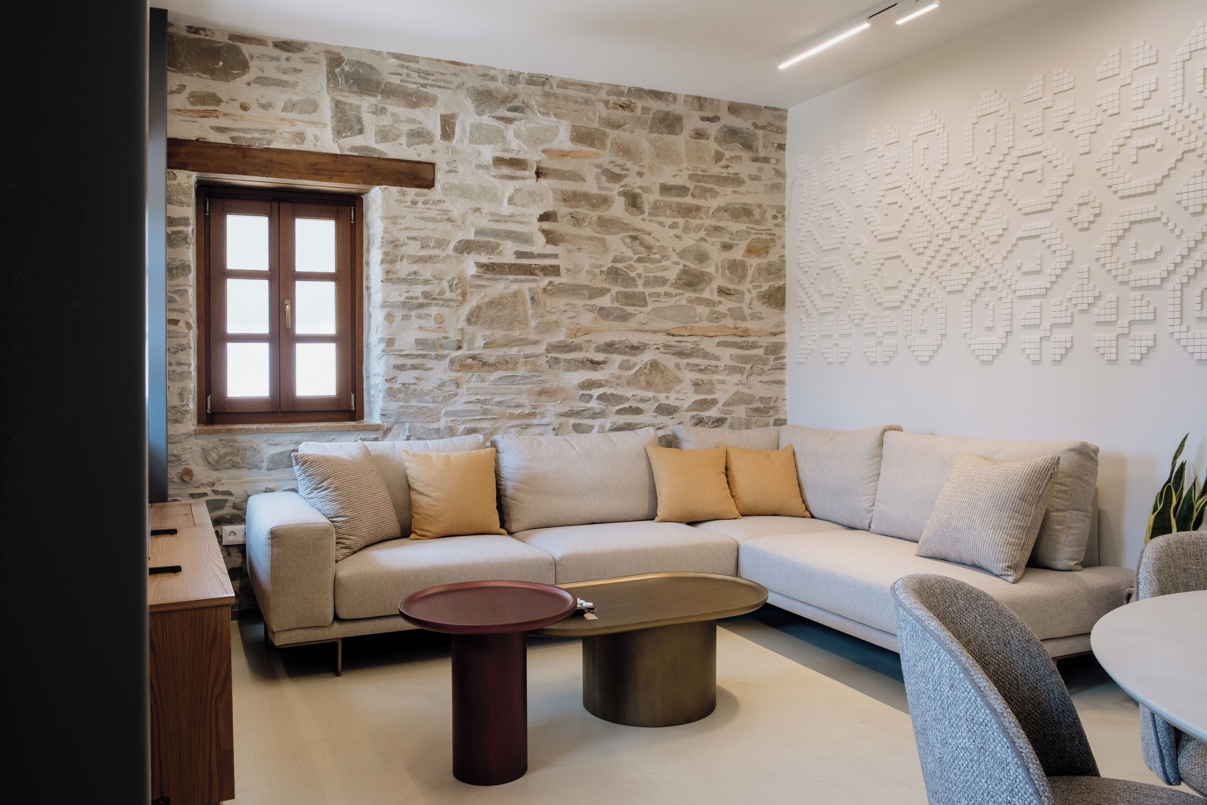 A modern living room with a stone wall, a wooden-framed window, a beige sofa, and a round coffee table.