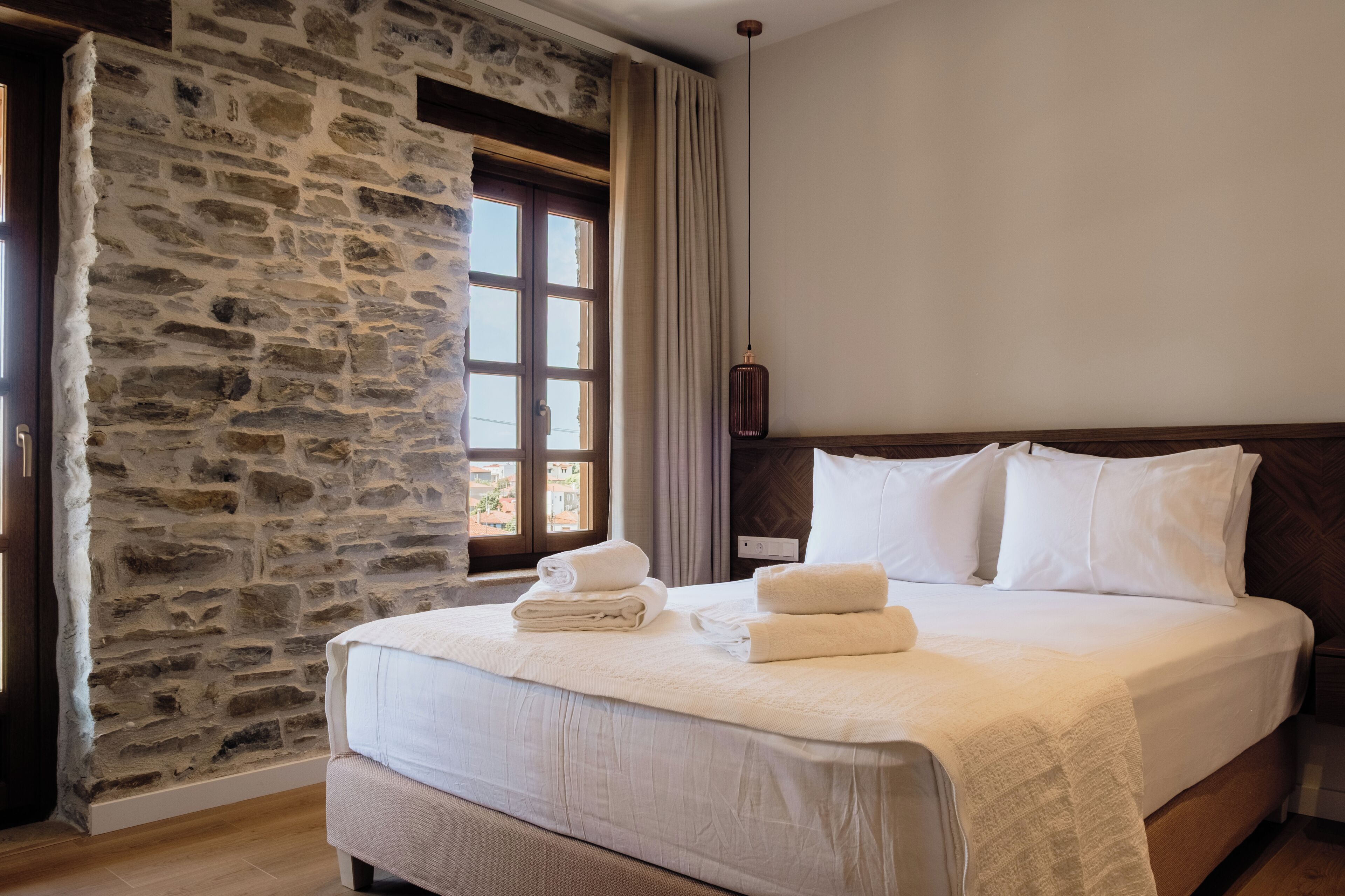 A hotel room with a stone wall, a bed with white linens, and a window with curtains.