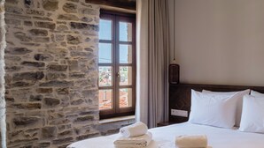 Ein Schlafzimmer mit Steinwand, einem großen Fenster, einem Bett mit weißen Leinen und einer hängenden Leuchte.