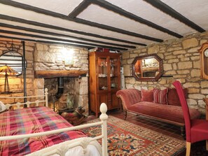 A room with a stone wall, a wooden cabinet, a red sofa, a patterned rug, and a bed with a plaid blanket. - The Annexe at Cherry Cottage (Gloucester)