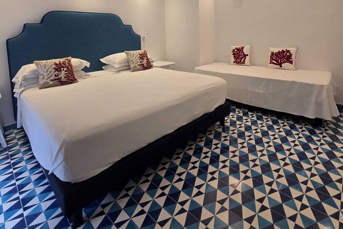 A hotel room with two beds, a geometric patterned floor, and wall-mounted lighting.