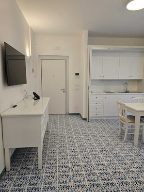 A compact kitchen with white cabinets, a sink, and a dining area with a chair. - Palmerie Luxury Apartments (Capaccio-Paestum)