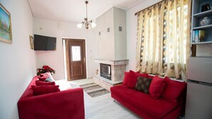 Una sala de estar con un sofá rojo, una chimenea, un televisor y una puerta que da a otra habitación.
