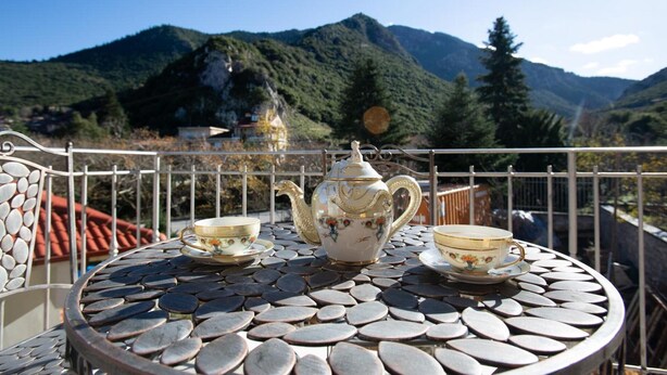 Una mesa metálica redonda con una tetera y tazas, frente a un paisaje montañoso.