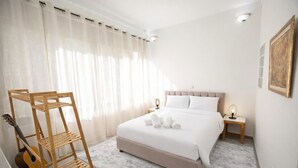Un dormitorio con una cama, una guitarra, un perchero de madera, una mesita de noche y una lámpara.