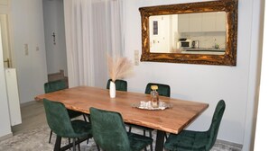 Un comedor con mesa de madera, sillas tapizadas de verde, un jarrón decorativo y un espejo en la pared.