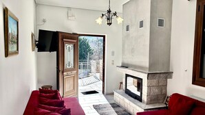 A living room with a fireplace, red sofas, and a view of the outside. - Gravias Villa with Fireplace and Barbecue, Mountain and River Views (Γραβιά)