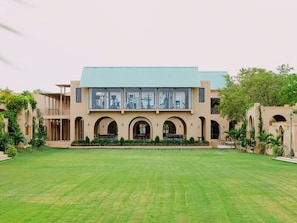 A building with a large lawn in front, multiple arched windows, and a flat roof. - Nirva Club and Resort by Siara (Modasa)