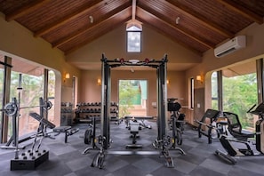 A gym with various exercise equipment, large windows, and a wooden ceiling. - Nirva Club and Resort by Siara (Modasa)