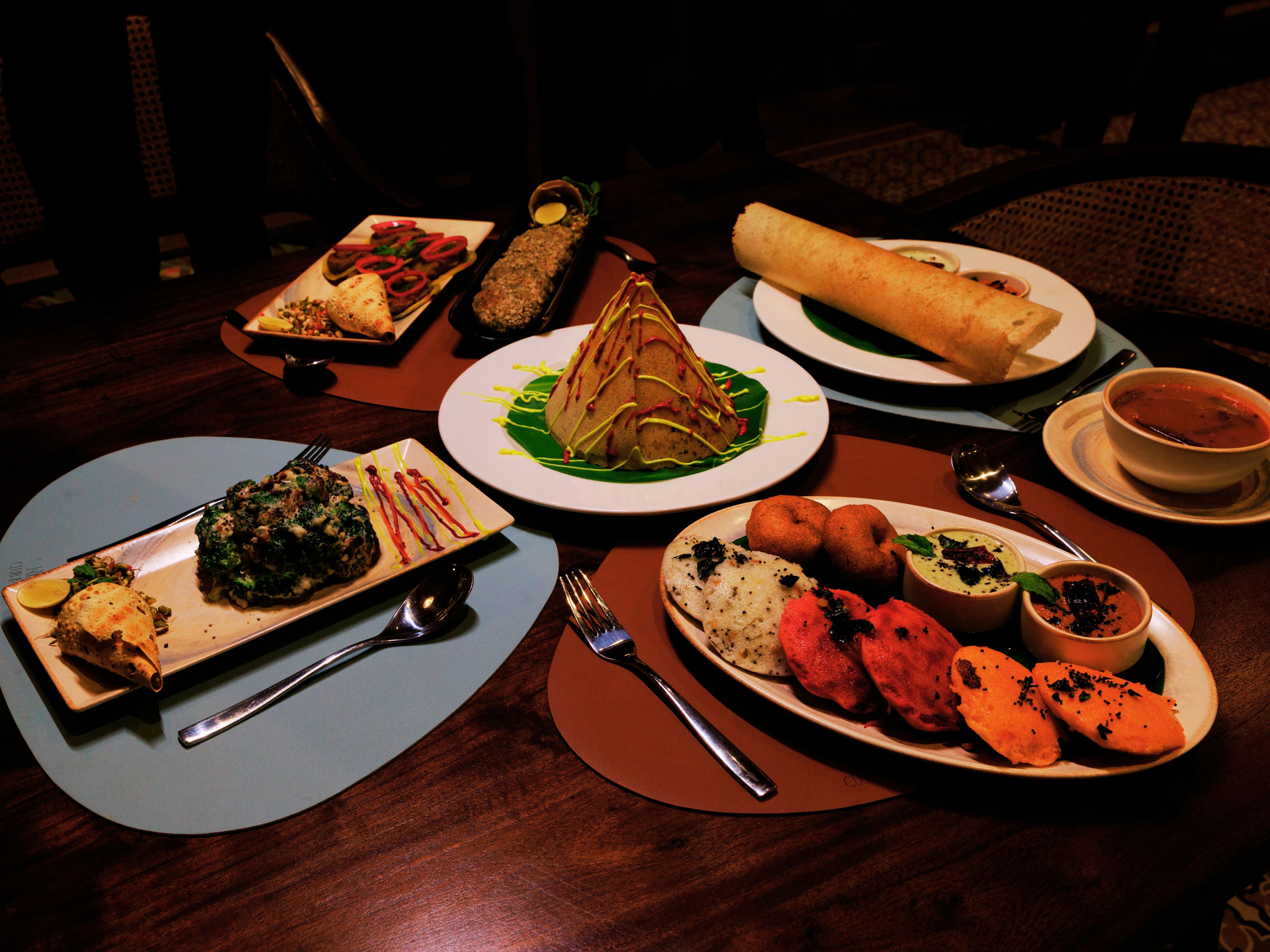 A variety of dishes on a dining table, including a rolled bread, a bowl of soup, and several plates with different foods.