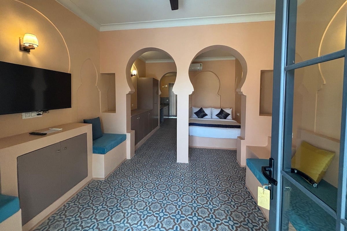 Una habitación de hotel con televisión, cama con almohadas, escritorio con silla y suelo estampado.