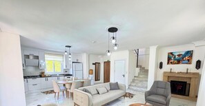 Un salon moderne avec un canapé, des fauteuils, une table à manger et une cuisine en arrière-plan.