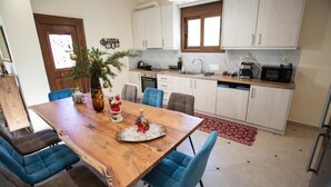 Een keuken met witte kasten, een houten eettafel met blauwe stoelen, een potplant en een rood kleed.