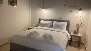Een net opgemaakt bed met opgevouwen handdoeken, een grijs beklede hoofdbord, nachtkastjes met lampen en een decoratieve wand met vlinderstickers.