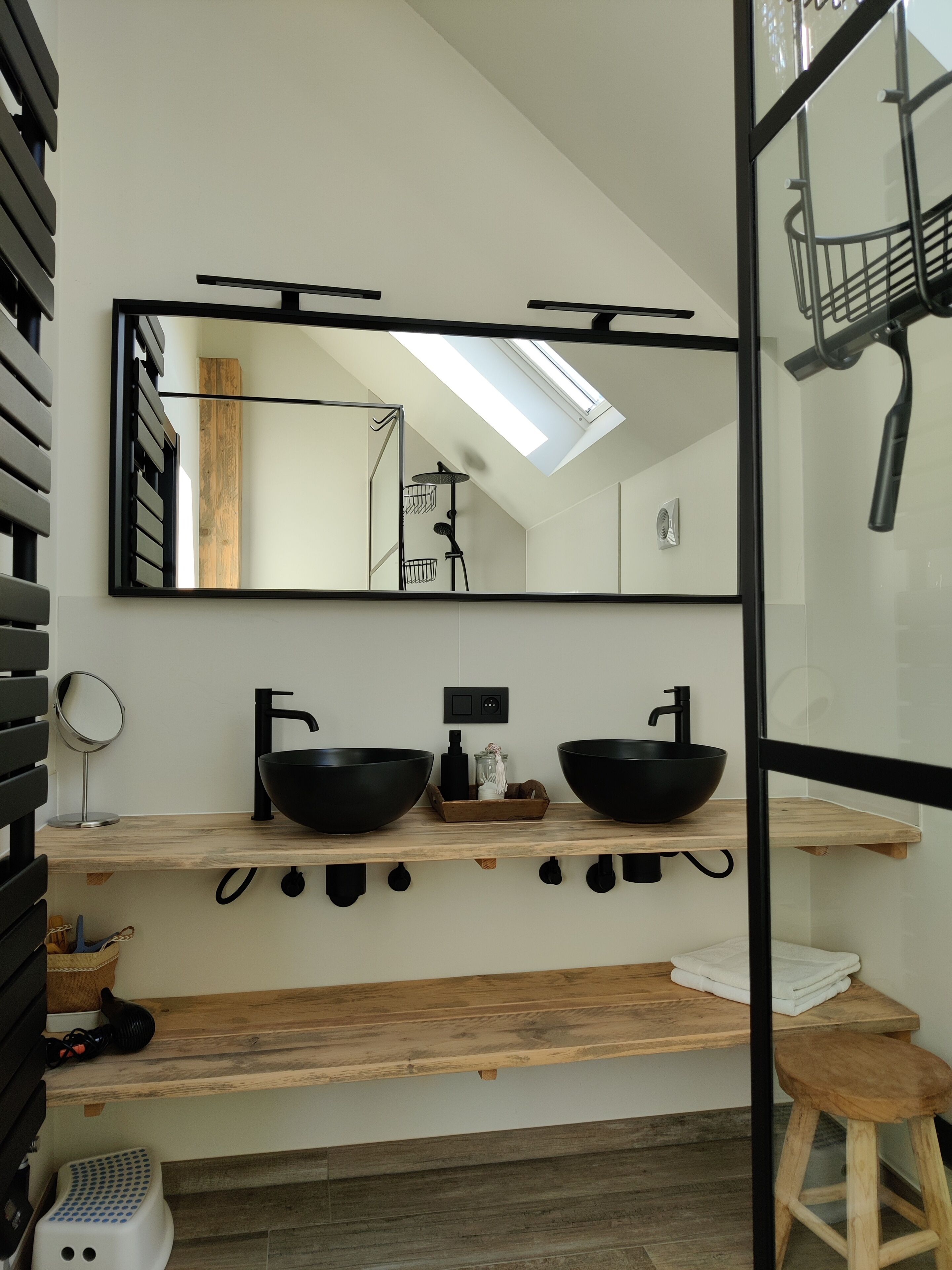 Une salle de bain moderne dotée d’un puits de lumière, de deux lavabos noirs, d’un meuble-lavabo en bois et d’un miroir.