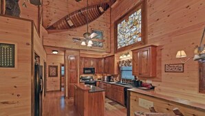 A wooden interior with a kitchen, dining area, and a large stained glass window. - A River Runs Through It by Chatuge Home Concierge | Private Riverfront · Rustic Luxury Cabin · Fireplace · Deck Views · Kayak & Fish Access (Hayesville)