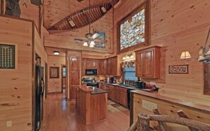 A wooden interior with a kitchen, dining area, and a large stained glass window. - A River Runs Through It by Chatuge Home Concierge | Private Riverfront · Rustic Luxury Cabin · Fireplace · Deck Views · Kayak & Fish Access (Hayesville)