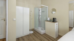 A hotel room with a walk-in closet, a glass-enclosed shower, a small cabinet with a coffee maker, and a mirror on the wall. - Lisbon Uptown Rooms by Homing (Lisbon)