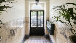 A marble-floored hallway with a black door, a hanging lantern, and potted plants. - Lisbon Uptown Rooms by Homing (Lisbon)