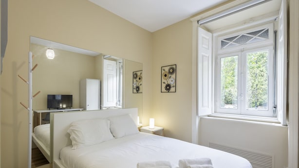 A bedroom with a bed, a bedside table, a mirror, a window, and artwork on the wall. - Lisbon Uptown Rooms by Homing (Lisbon)