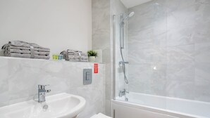 Moderni kylpyhuone, jossa on pesuallas, wc ja lasiseinällä varustettu suihku.
