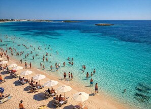 A beach with clear turquoise water, people swimming and walking, and sun loungers with umbrellas. - Aura Studio in Torre Lapillo – Wi-Fi, Air Conditioning, and Garden (Boncore)
