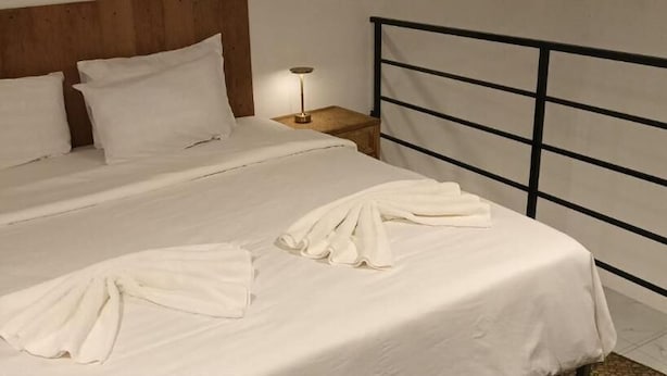 A bed with white linens and a metal headboard, a bedside table with a lamp, and a wooden headboard. - Reaksa Hostel Koh Rong (Koh Rong)