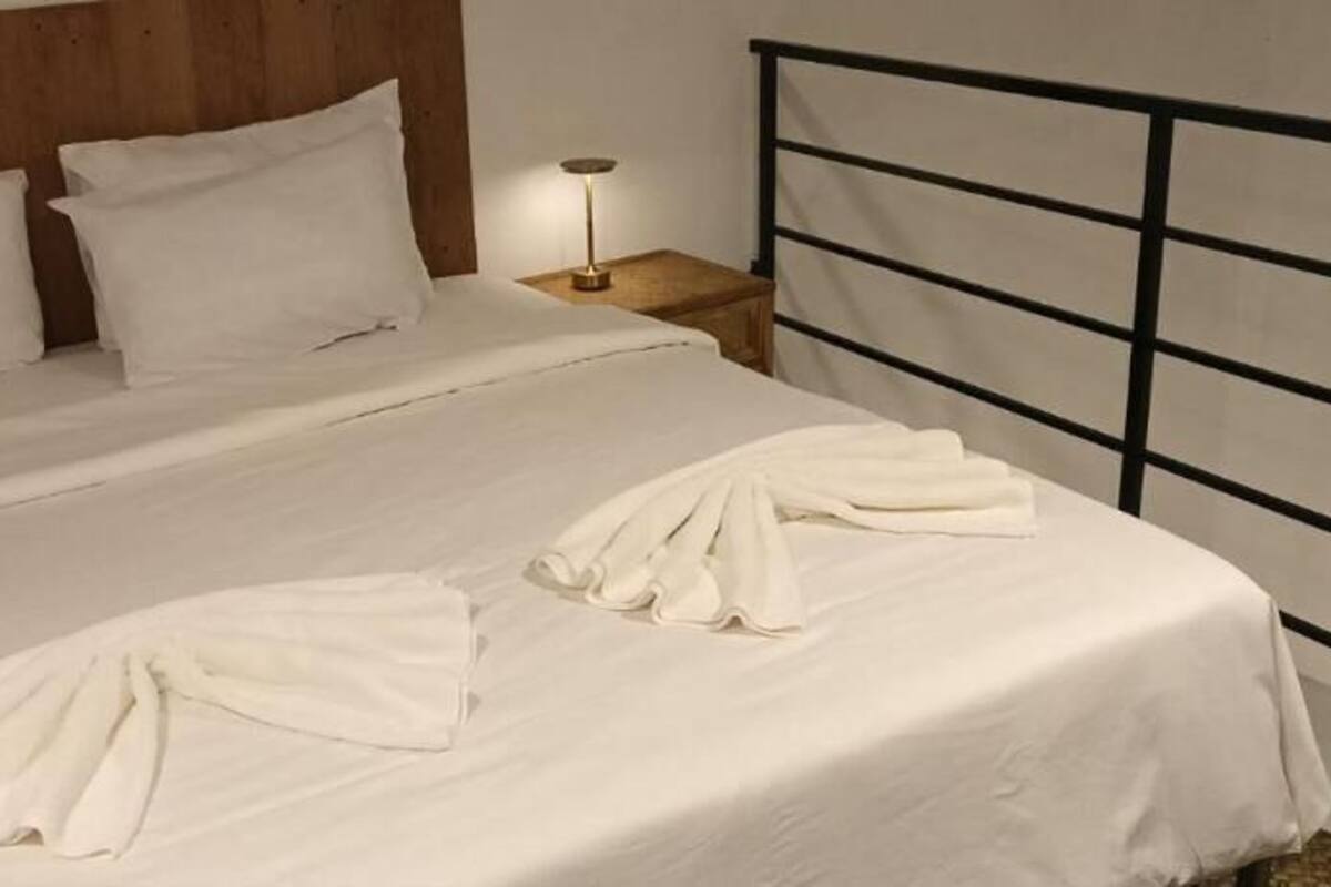 A bed with white linens and a metal headboard, a bedside table with a lamp, and a wooden headboard.