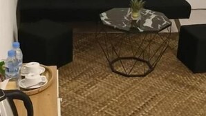 A room with a black sofa, a glass coffee table with a pineapple, a wooden side table with a kettle, and a tiled floor. - Reaksa Hostel Koh Rong (Koh Rong)