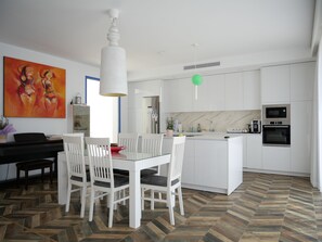 A modern kitchen with white cabinets, a central island, and a dining area with white chairs. - Super modern villa located 10 minutes by car from Palma city centre and Portixol (Palma de Mallorca)