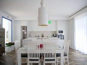 A modern kitchen with white cabinetry, a central island, and a dining area with white chairs. - Super modern villa located 10 minutes by car from Palma city centre and Portixol (Palma de Mallorca)