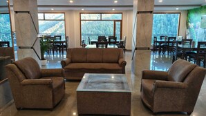 A spacious lobby with a brown sofa set, a glass coffee table, and a dining area with tables and chairs. - Summer hill resort (Shimla)