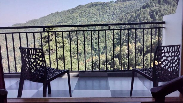 A balcony with a view of a forested hillside, two chairs, and a railing. - Summer hill resort (Shimla)