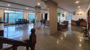 A spacious lobby with a staircase, a reception desk, seating area, and large windows. - Summer hill resort (Shimla)