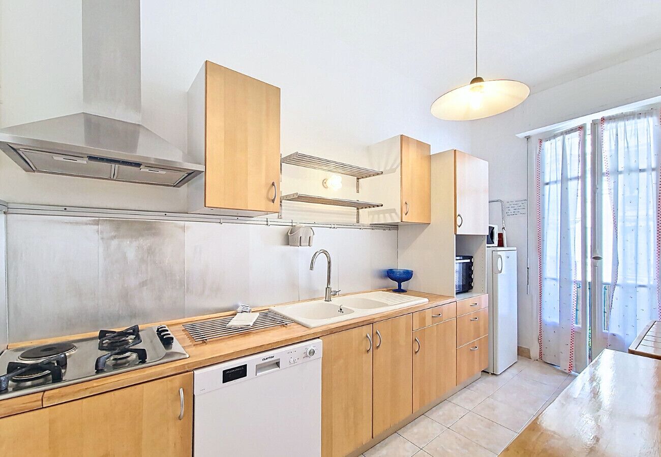A modern kitchen with a stove, sink, and dishwasher, wooden cabinets, and a window with curtains.