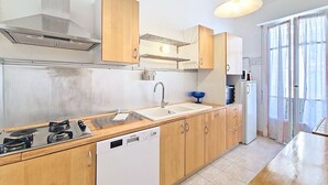 A modern kitchen with a stove, sink, and dishwasher, wooden cabinets, and a window with curtains. - New! N&J -LE CATINAT - Spacious - Balcony (Nice)
