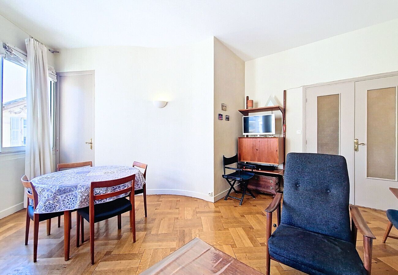 A room with a dining table, chairs, a television, and a wardrobe.